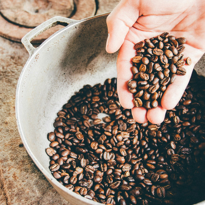 Coffee beans in a gray steel wok, the kind of pan used for stovetop roasting at home
