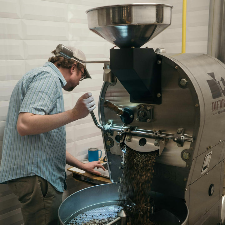 A roaster working at the drum of a commercial coffee roasting machine during a production roast day - Inheritance Coffee, Pensacola, FL