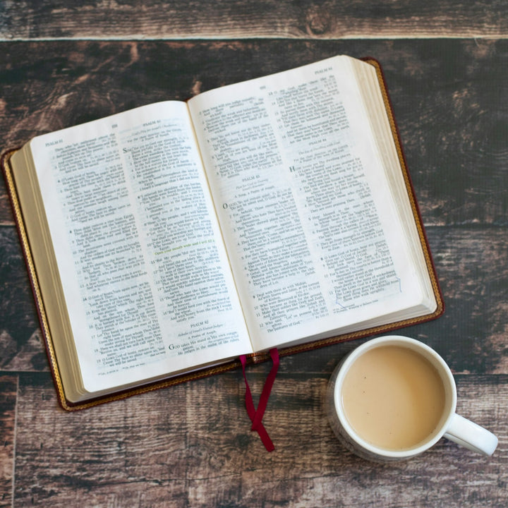 An open Bible beside a white ceramic coffee mug