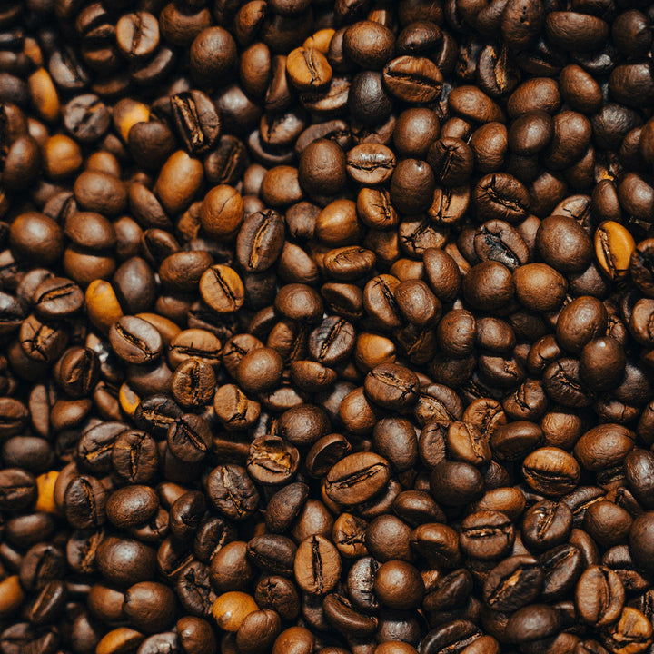 A dense pile of roasted coffee beans filling the frame, showing the surface texture of each bean - Inheritance Coffee, Pensacola, FL roaster for home brewers and cafes
