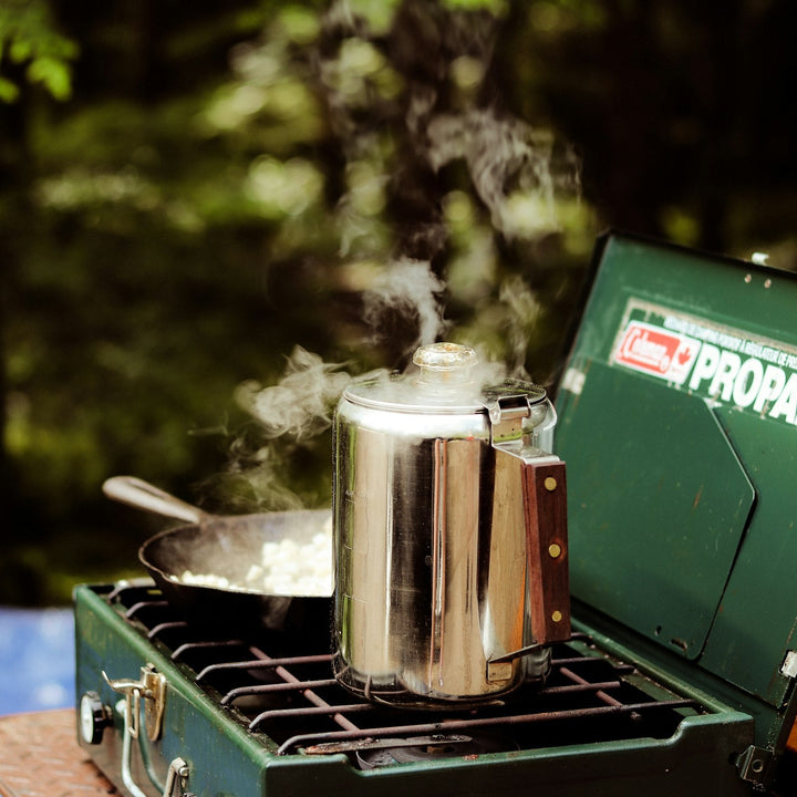 A metal pot of coffee heating over a camp stove, with steam rising