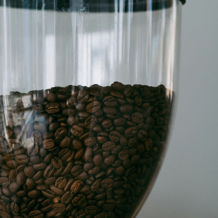 A manual coffee grinder surrounded by whole roasted coffee beans