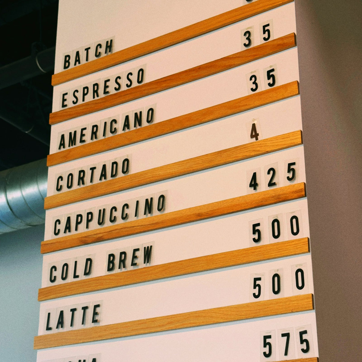 A cafe menu board of wooden rails and black plastic letters listing each drink as its own priced line - Inheritance Coffee, Pensacola, FL
