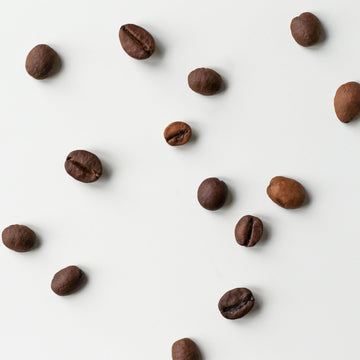 Brown roasted coffee beans spread in an even layer on a pale surface, seen from above.
