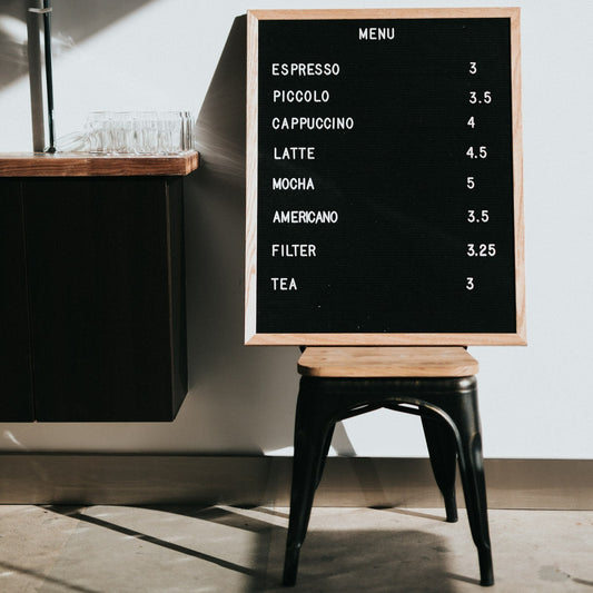 Coffee shop menu board listing espresso drinks with prices beside a wooden counter