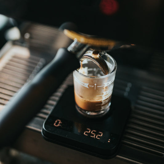 Espresso extracting into a glass on a digital bar scale showing the shot weight
