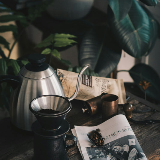 A black single-dose burr grinder on a kitchen counter beside a stainless steel kettle