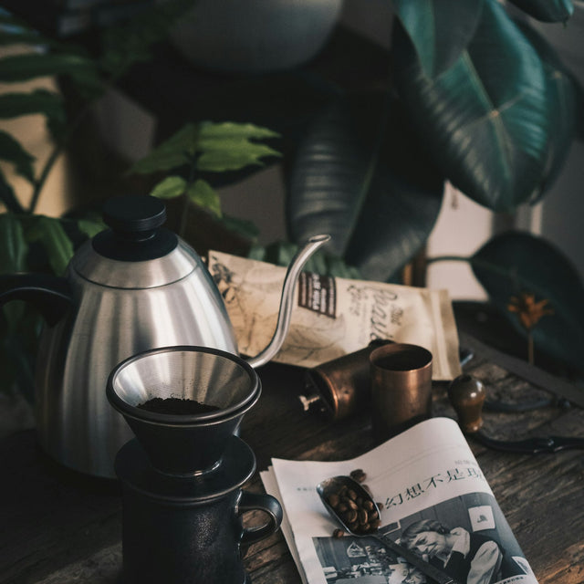 A black single-dose burr grinder on a kitchen counter beside a stainless steel kettle