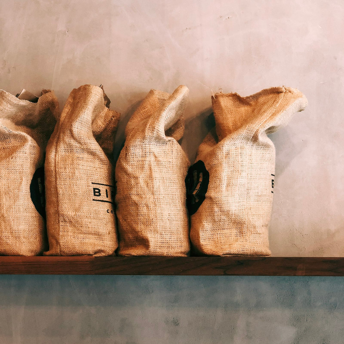 Four burlap sacks of coffee beans lined up on a shelf in a coffee shop - Inheritance Coffee, Pensacola, FL roaster for cafes, churches and coffee startups