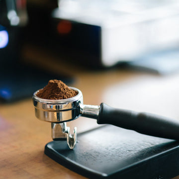 Portafilter holding a weighed dose of ground coffee resting on a bar scale