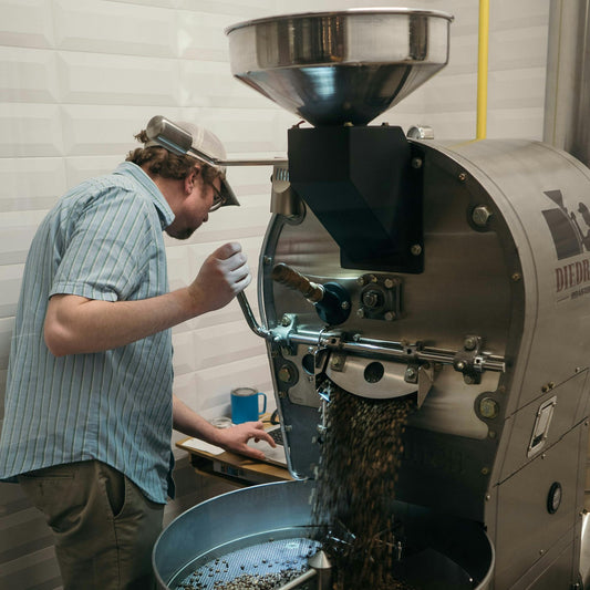 A roaster working at the drum of a commercial coffee roasting machine during a production roast day