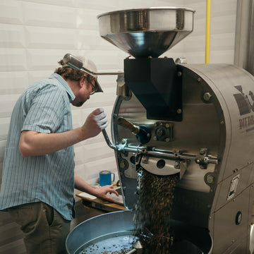 An operator at the controls of a commercial drum coffee roaster in a small roastery
