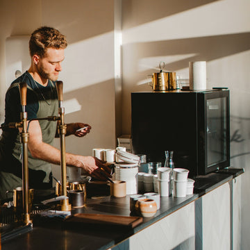 Barista working an espresso bar with grinder, scale and cups within reach on the counter
