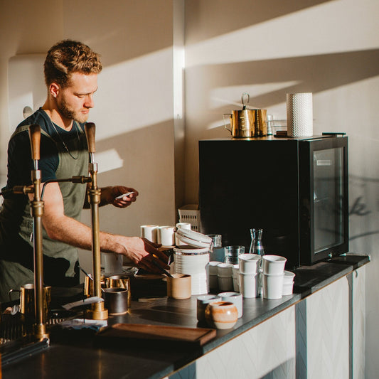 Barista working an espresso bar with grinder, scale and cups within reach on the counter