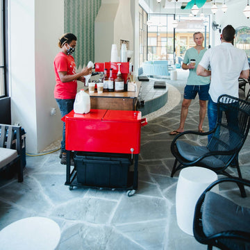 Volunteer staffing a mobile espresso cart in a church lobby between services