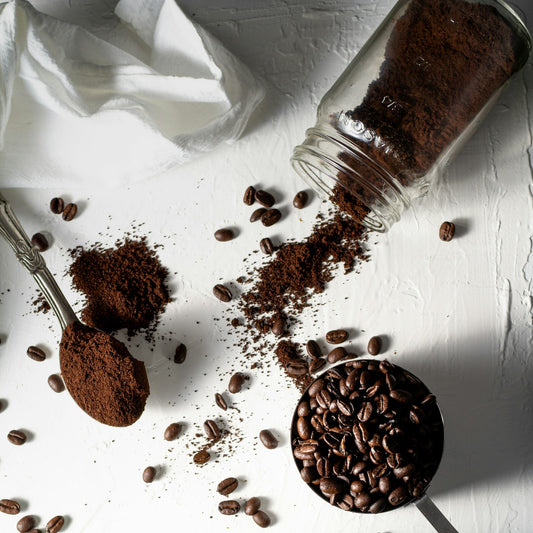 Whole roasted coffee beans and freshly ground coffee laid out beside a cup of black coffee on a white surface