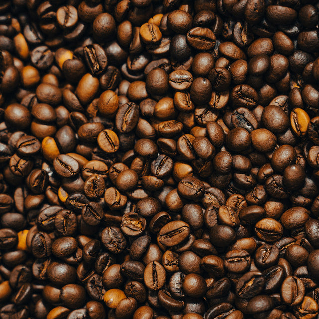 A dense pile of roasted coffee beans filling the frame, showing the surface texture of each bean - Inheritance Coffee, Pensacola, FL roaster for home brewers and cafes
