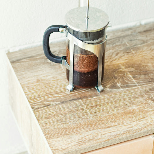 A French press coffee maker on a wooden table, the most common immersion coffee brewer