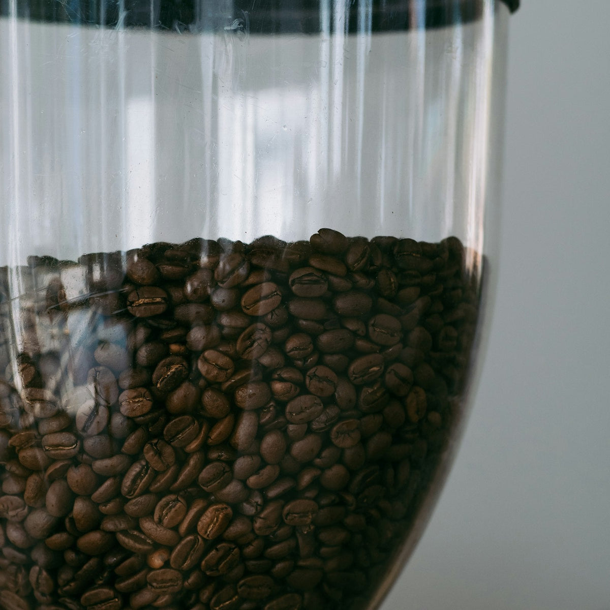 A manual coffee grinder surrounded by whole roasted coffee beans