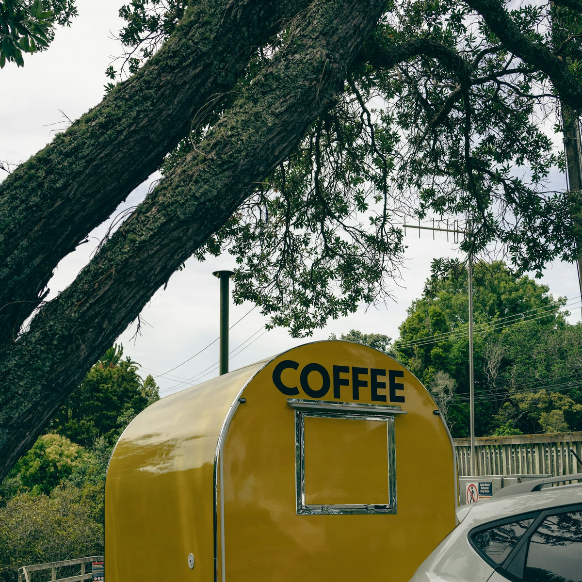 a yellow coffee trailer parked outdoors next to a car
