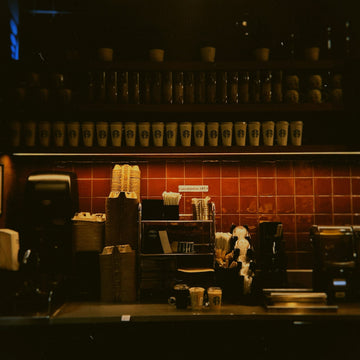A coffee brewing machine and stacked cups on a commercial coffee shop service counter
