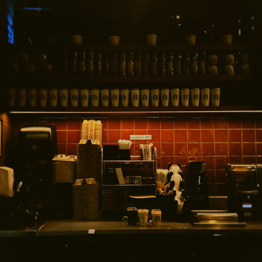 A coffee brewing machine and stacked cups on a commercial coffee shop service counter