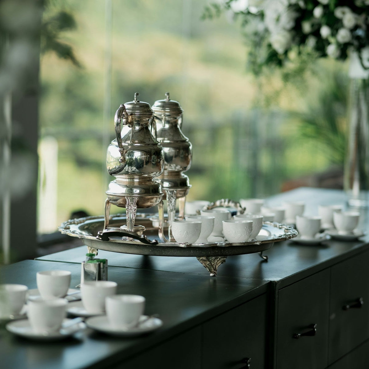 A silver coffee service set with cups and saucers laid out on a table