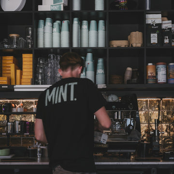 A barista working behind the counter of a small coffee bar with the espresso machine beside them