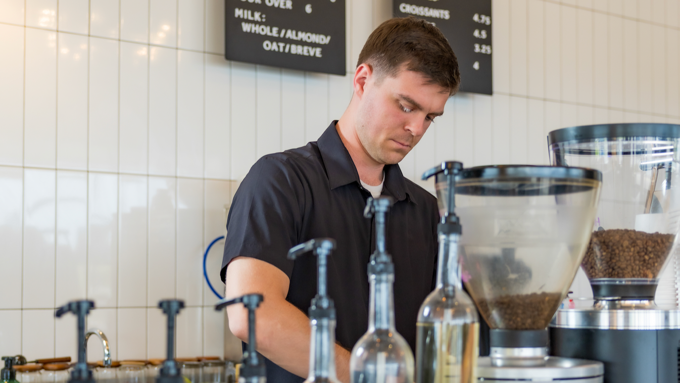 Barista working behind a counter with coffee-making equipment and drinks.