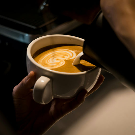 Latte with latte art served in a white cup, made with ASCENT coffee, roasted by Inheritance Coffee in Pensacola, FL for home brewers and cafes