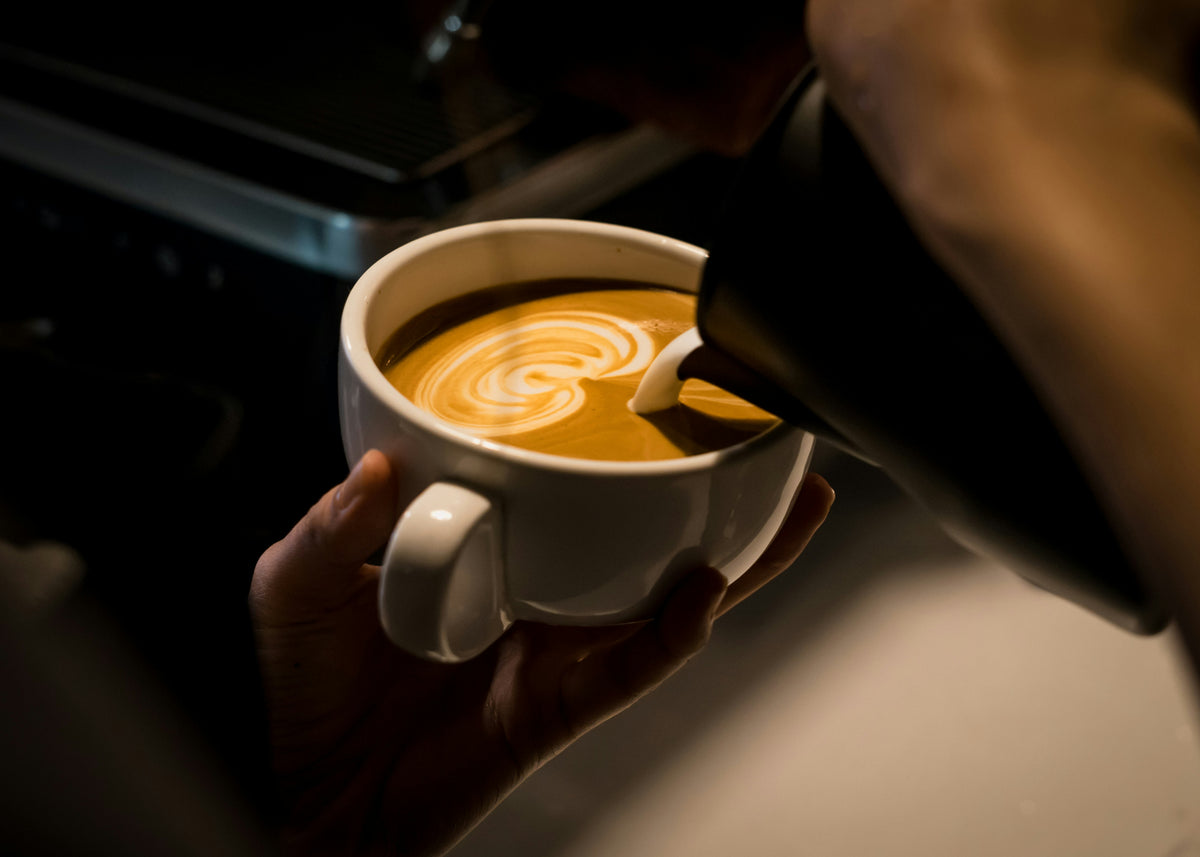 Latte with latte art served in a white cup, made with ASCENT coffee, roasted by Inheritance Coffee in Pensacola, FL for home brewers and cafes